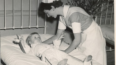 A nurse leaning over a young male patient wearing callipers.