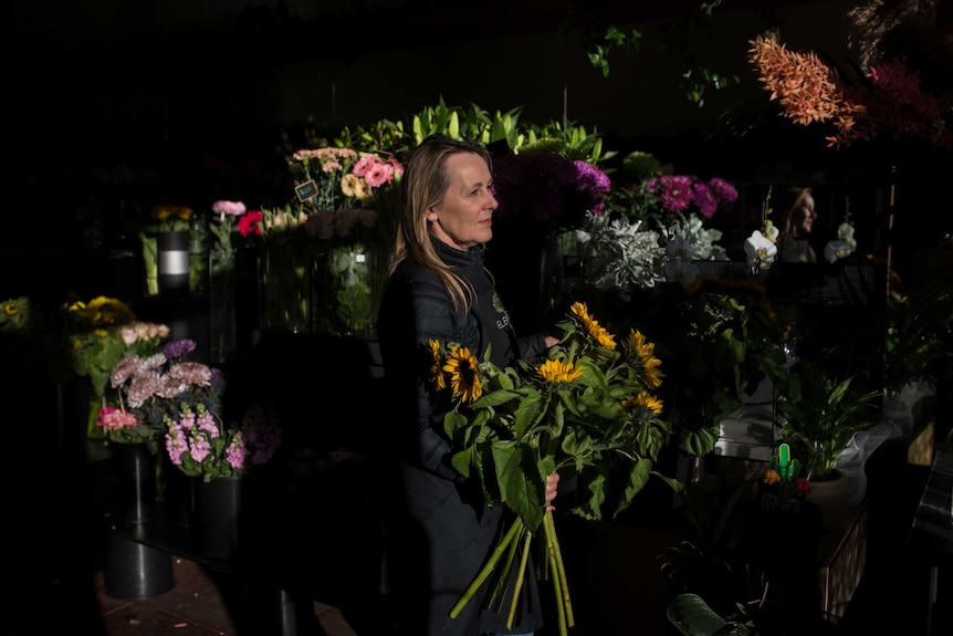 Helen holds a bunch of sunflowers as sun beams in through her florist shop window