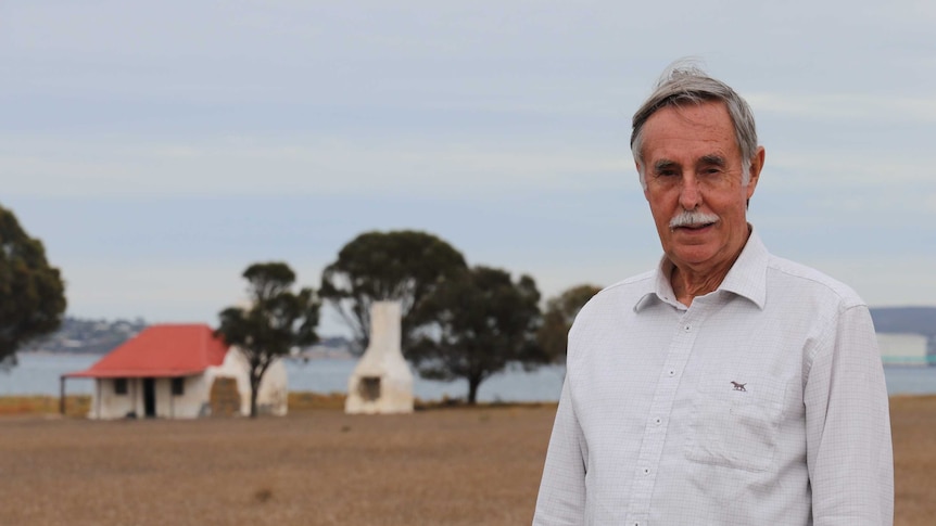 Man standing in foreground middle right, whitewash stone cottage in background left