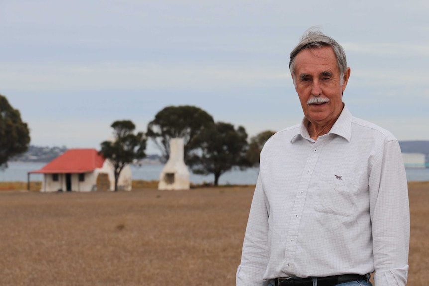 Man standing in foreground middle right, whitewash stone cottage in background left