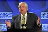 Clive speaks at a podium in front of a blue National Press Club of Australia backdrop and gestures with his hands.