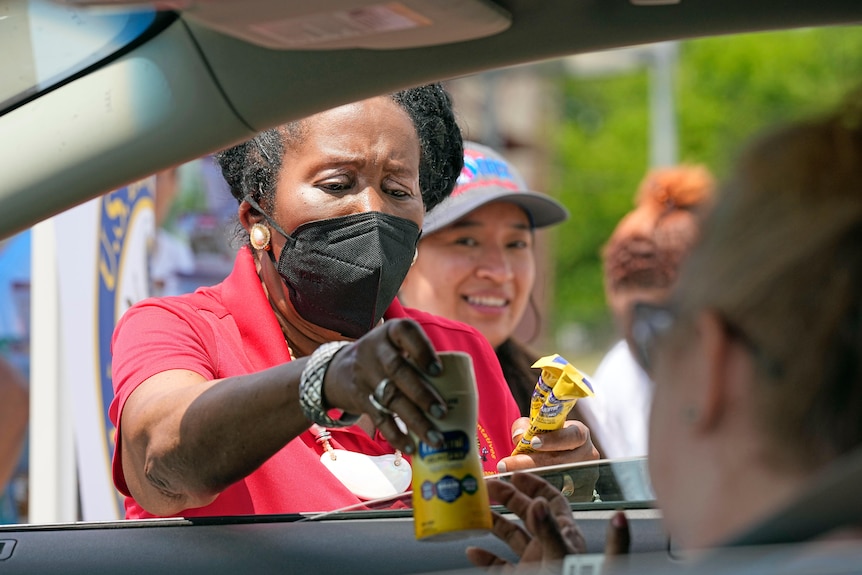 Sheila Jackson Lee in a black mask hands a bottle of baby formula through a car window