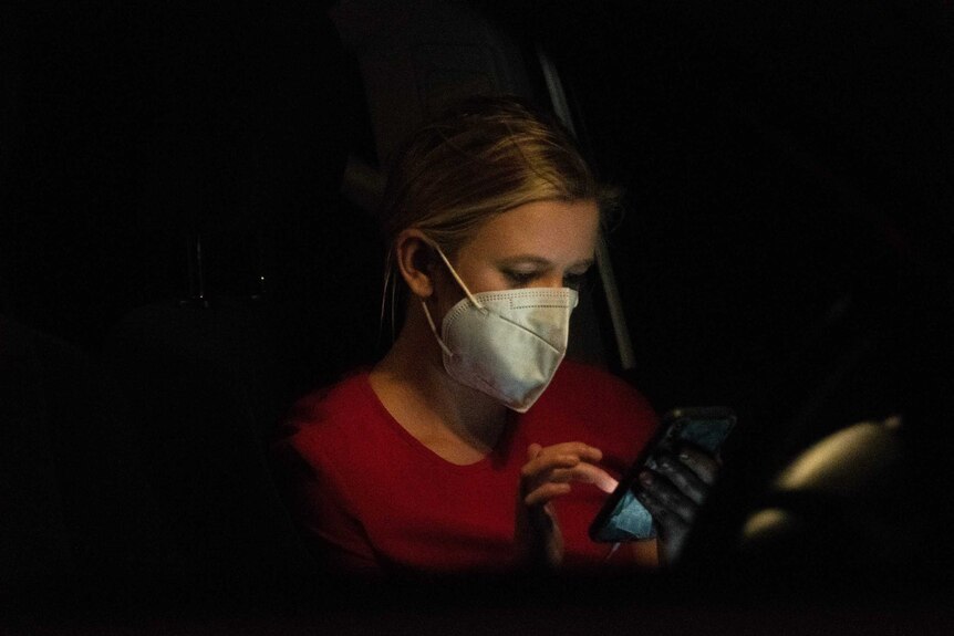 Night shot of woman wearing mask looking at mobile phone.