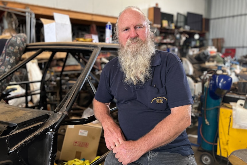 Man with long white beard sitting in front of car frame