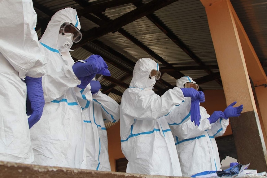 Health workers don purple gloves and protective suits