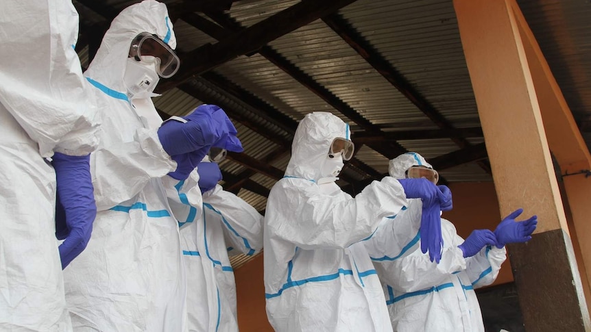Health workers don purple gloves and protective suits