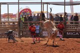 A bull rider moves away from a bucking bull surrounded by bull fighters in the rodeo arena in Mount Isa.