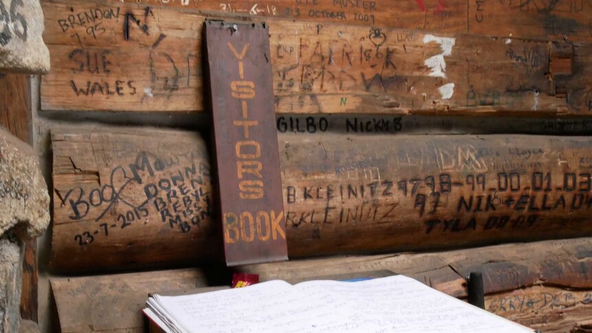 A visitors' book inside an alpine hut, also has visitors' names scratched into the walls
