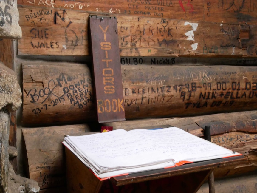 A visitors' book inside an alpine hut, also has visitors' names scratched into the walls