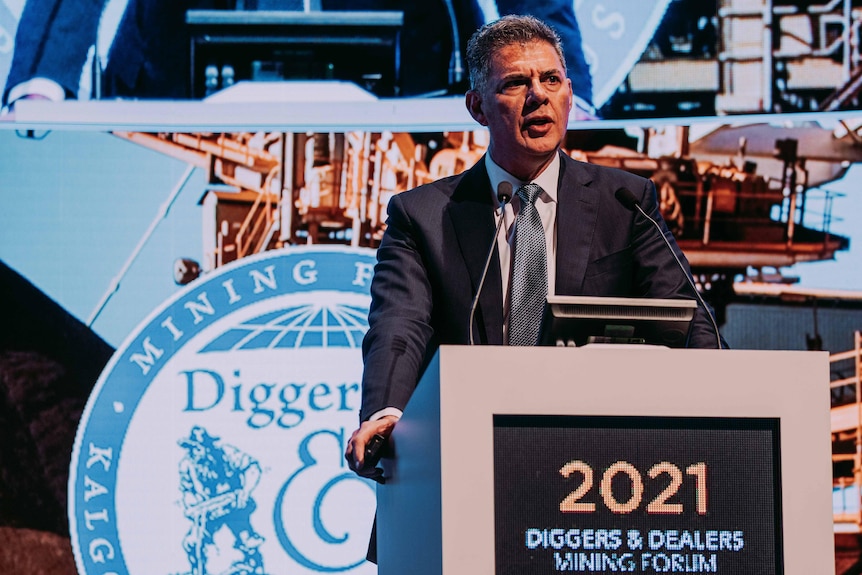 A man wearing a suit and tie speaking on stage behind a podium at a mining conference.  