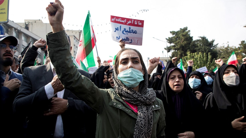 A woman in a face mask and head scarf raises a fist in the air amid a group of women. 