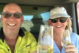A man and a woman sitting in a header cab holding champagne glasses and smiling.