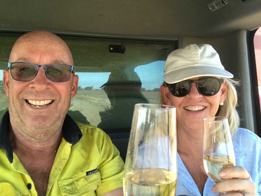 A man and a woman sitting in a header cab holding champagne glasses and smiling.