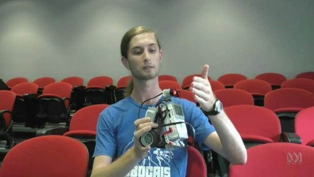 Man sits in theatre seating, holds robot in hands