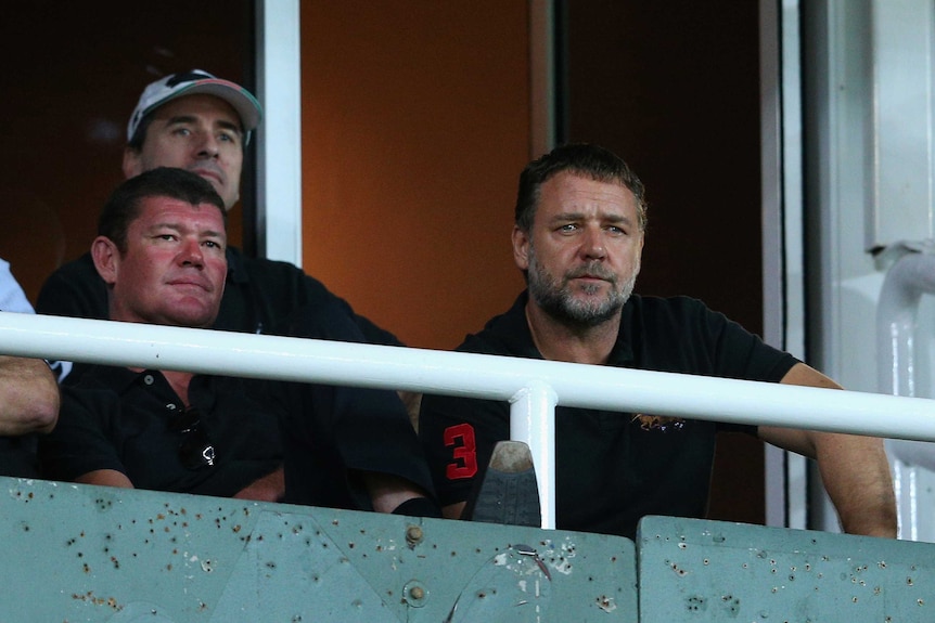 Three men sit in a stand staring intently ahead.