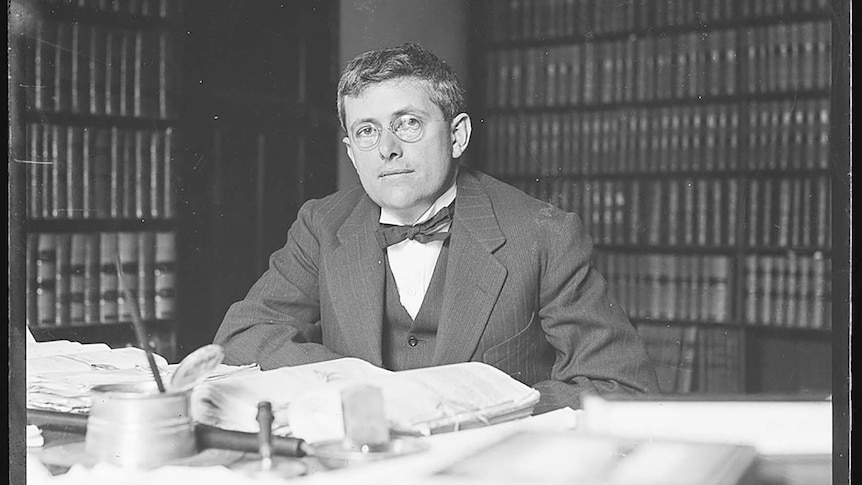 B&W photo of Doc Evatt at his desk with bookshelves full of law books behind him