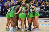 West Coast Fever Super Netball players gather in a huddle on court.