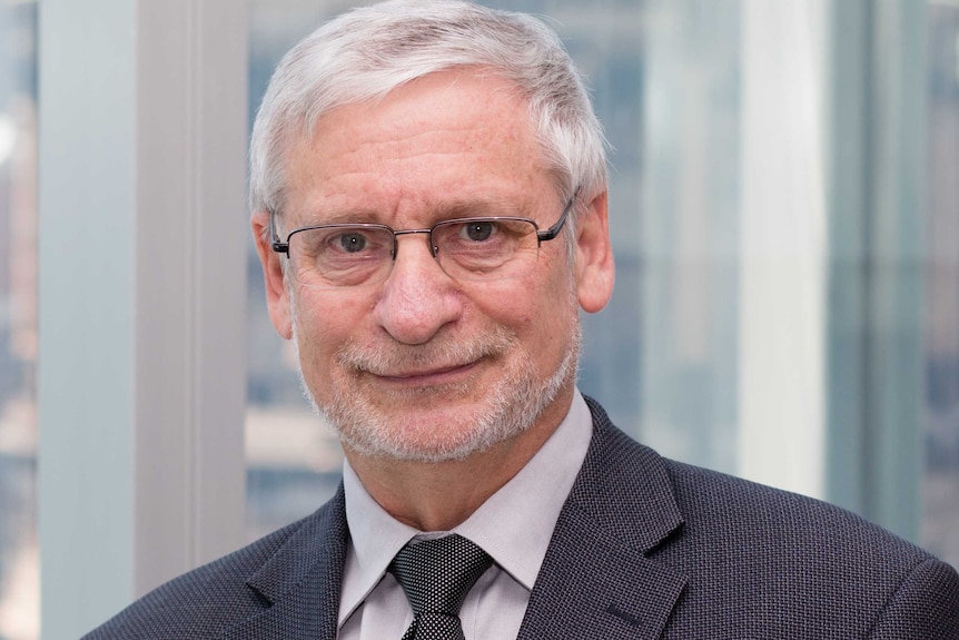 A photo of Arie Freiberg, who has white-grey hair and is wearing spectacles and dark suit