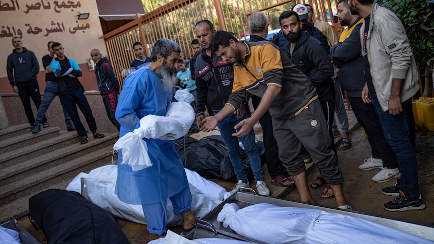 arab men crowding around body bags as one doctor hands one man a smaller body bag