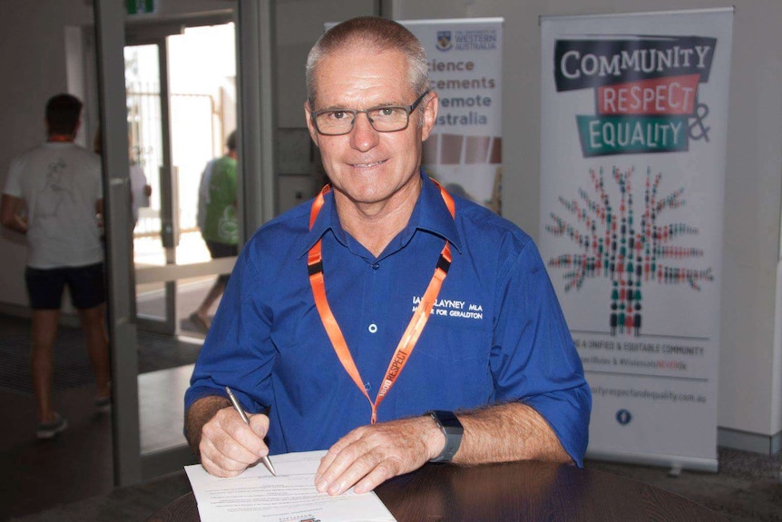 Ian Blayney sits at a dest wearing a blue shirt.