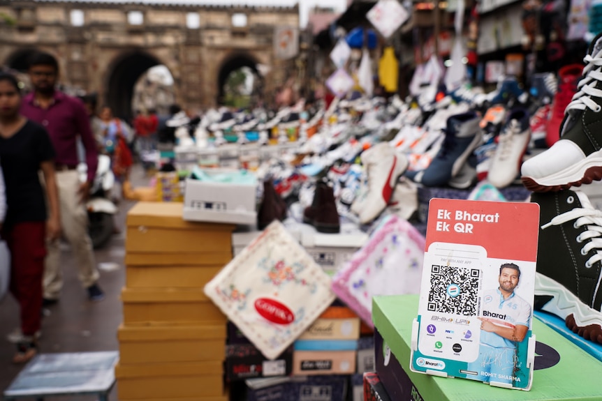 A sign with a QR code sits in the foreground of a shoe stall at a market