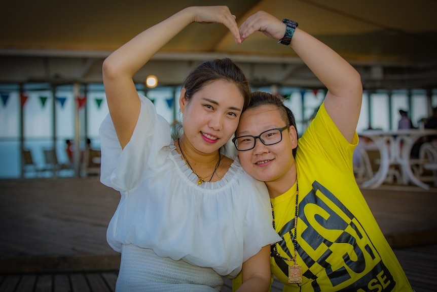 Two women hold their arms over their heads in the shape of a heart.