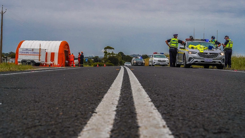 people wearing orange coloured uniforms and hi vis yellow uniforms stand on the side of a road next to police cars.