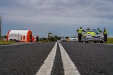 people wearing orange coloured uniforms and hi vis yellow uniforms stand on the side of a road next to police cars.