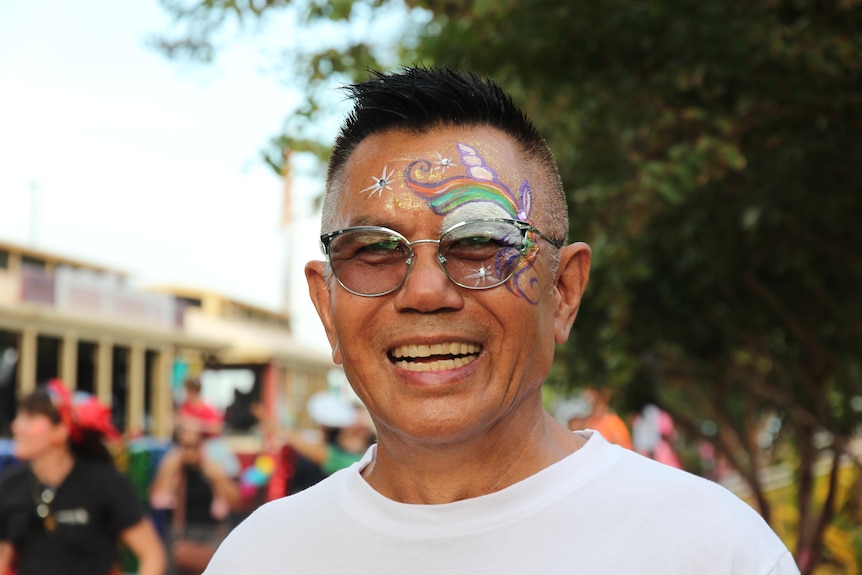 A man smiles with colourful face paint in the style of a unicorn.