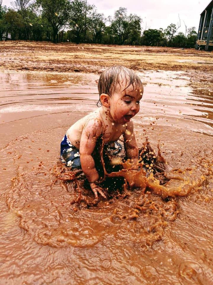 A toddler splashes happily in a muddy puddle of water