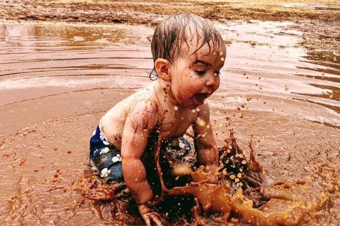 A toddler splashes happily in a muddy puddle of water