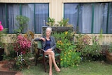 Jenny Sadar sitting on a chair in her her garden outside of her caravan 