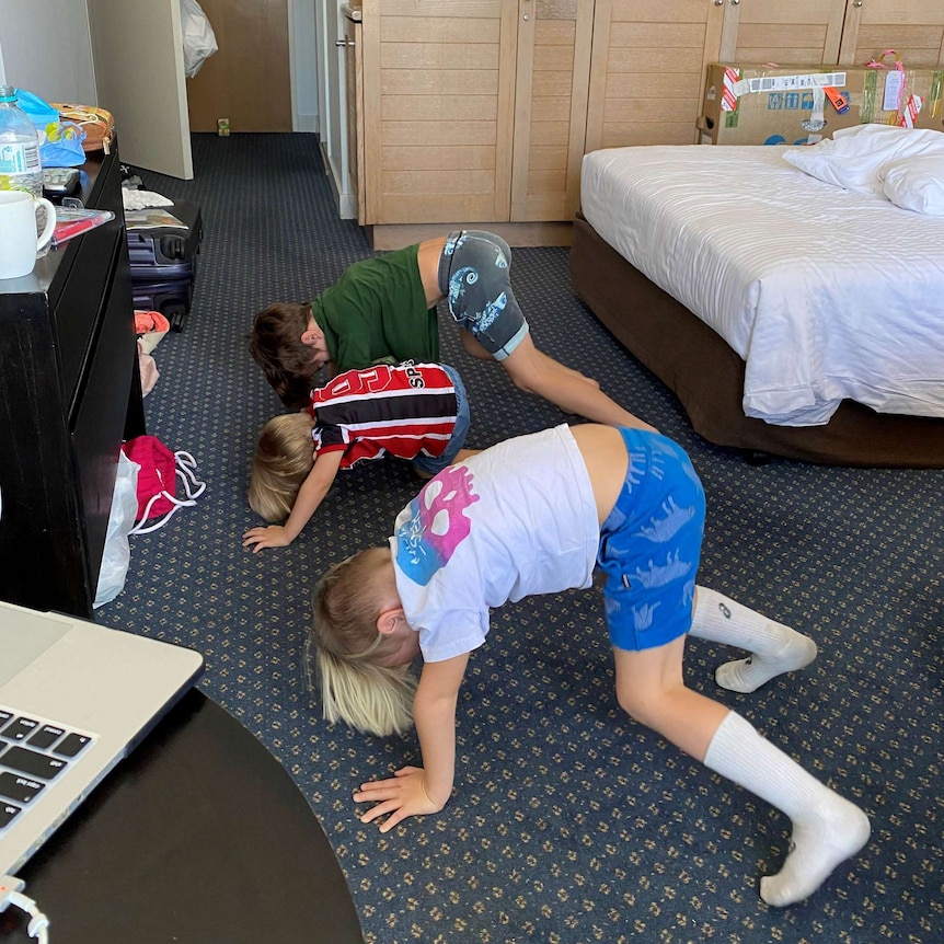 Three young boys do boot camp exercises in hotel quarantine.