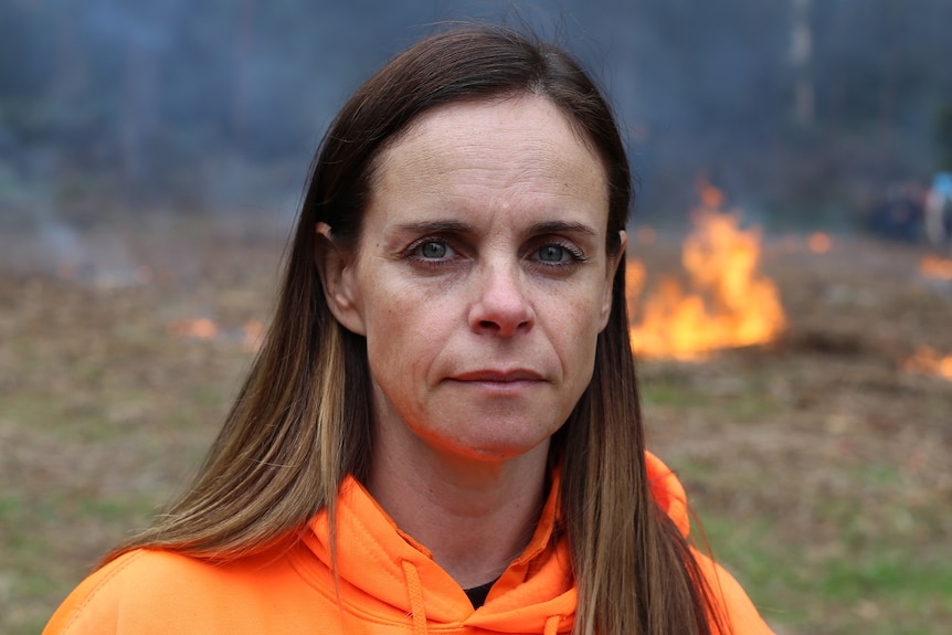 Mandy Nicholson stands in front of small glowing fires in bushland.