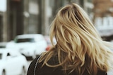 A woman with blonde hair walks along a street, her face is hidden from view.
