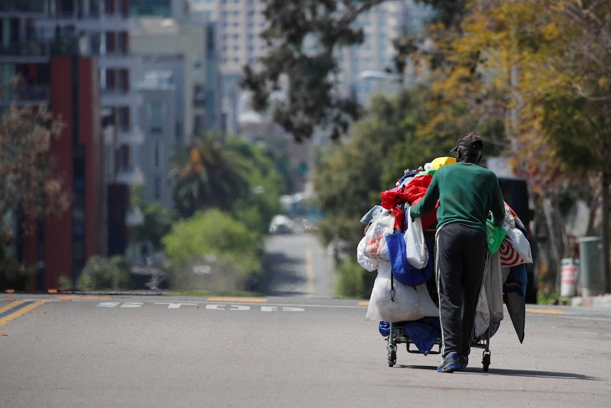 A homeless man pushes a cart full of his belongings along an empty street.