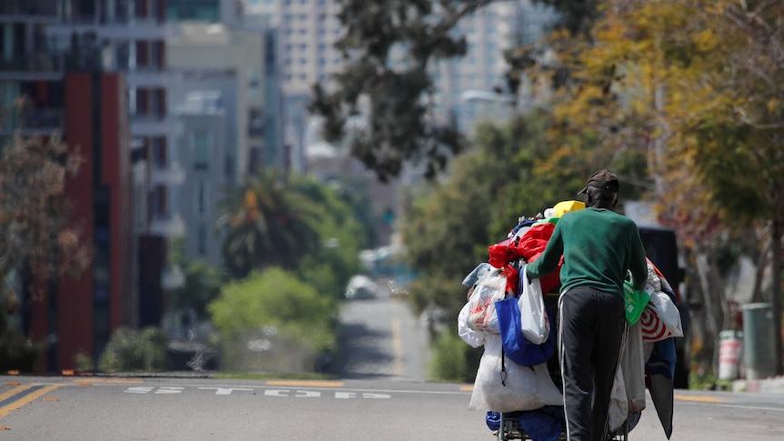 A homeless man pushes a cart full of his belongings along an empty street.
