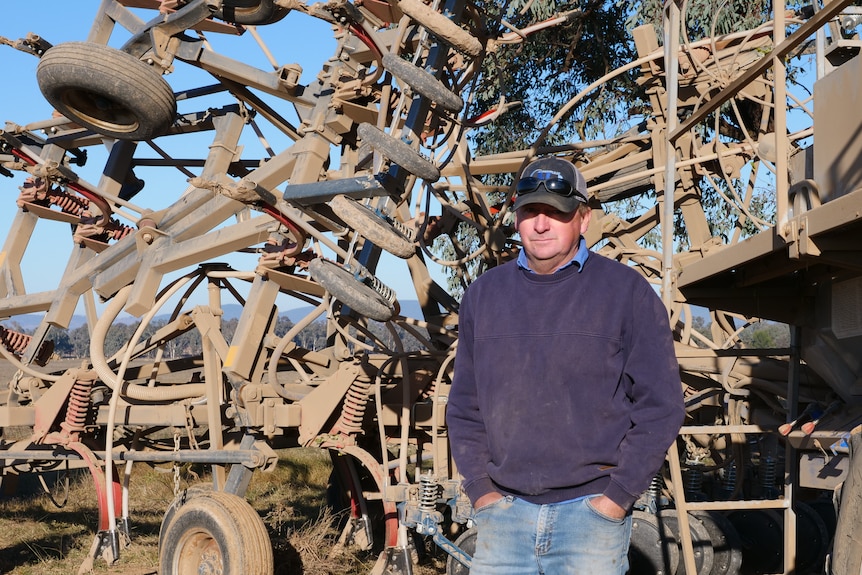 A man stands in front of a seeder. 