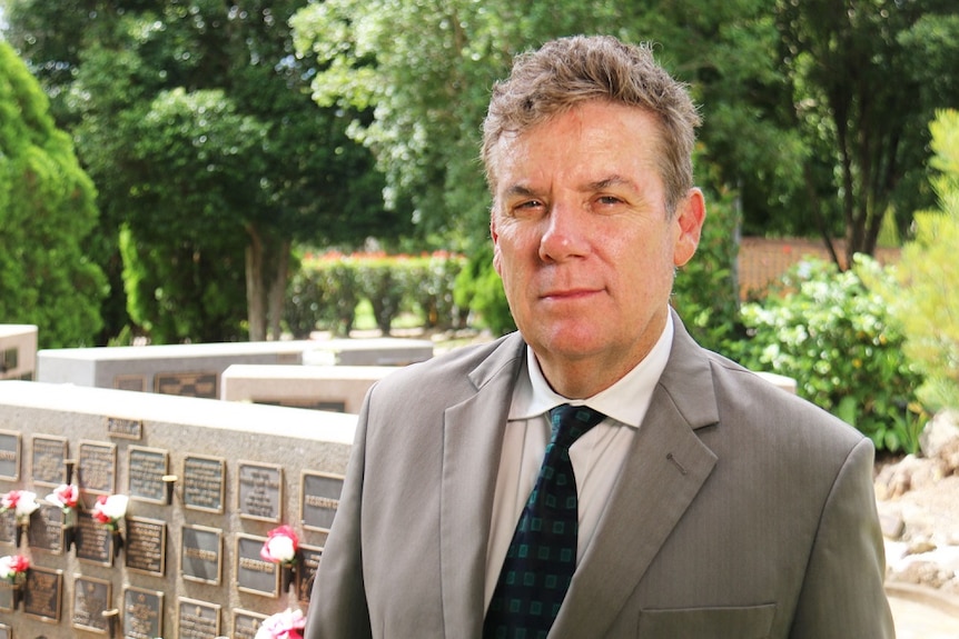 A man in a suit stands outside at a crematorium garden