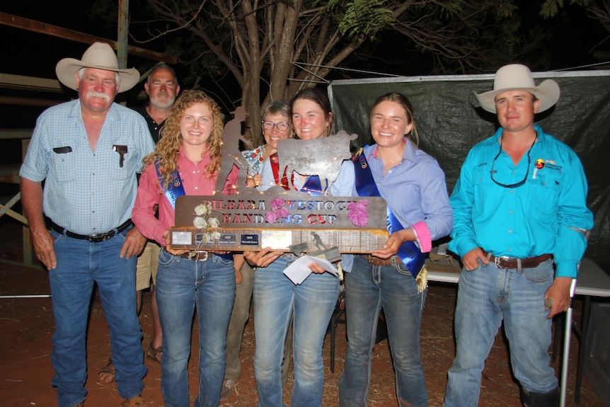 A group of stockwomen holding a trophy surrounded by judges