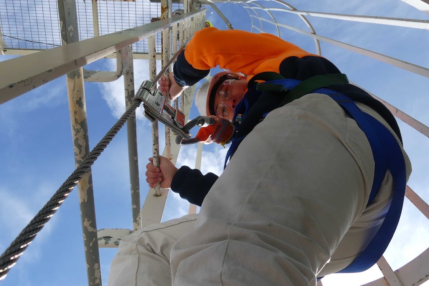 Migrant builder Huang Qinglong climbs a ladder wearing a harness