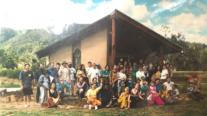 A group of people stand in front of a farm building with a pitched roof