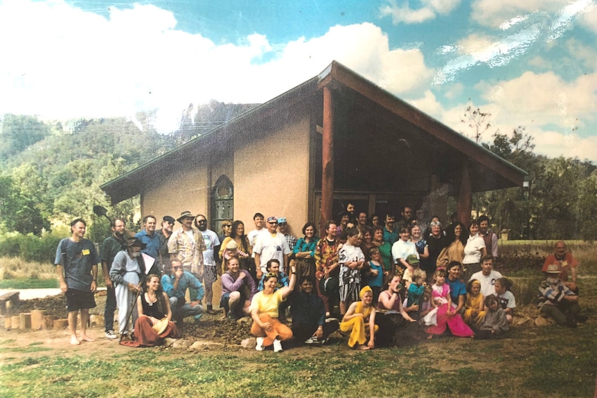 A group of people stand in front of a farm building with a pitched roof