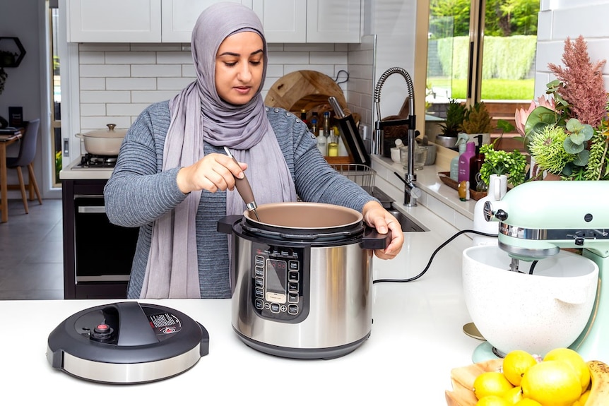 Lina Jebeile stands in the kitchen and looks down at her slow cooker while pretending to stir something in it.