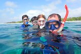 A man, woman and two children wearing scuba masks in the ocean with an island shore behind them