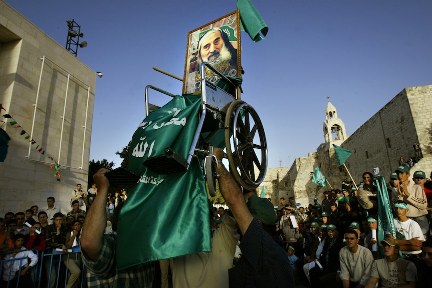 Wheelchair with photo of Ahmed Yassin held aloft above crowd.