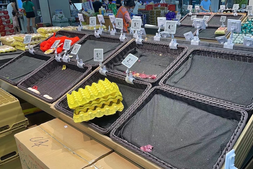 在一家中国超市内可以看到空荡荡的蔬菜摊，在 COVID 激增的情况下，兴奋的购物者将其挑选干净。