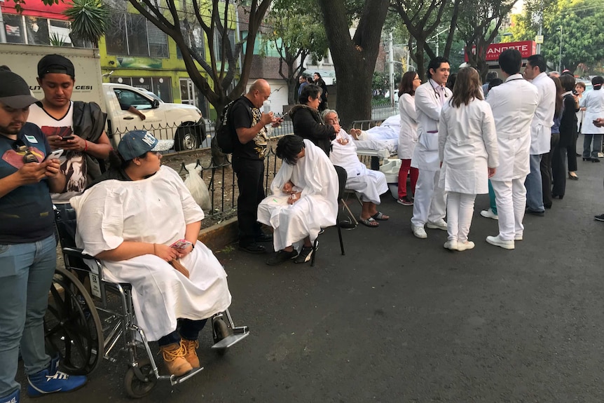 Medical staff and patients in white gowns stand on the street.