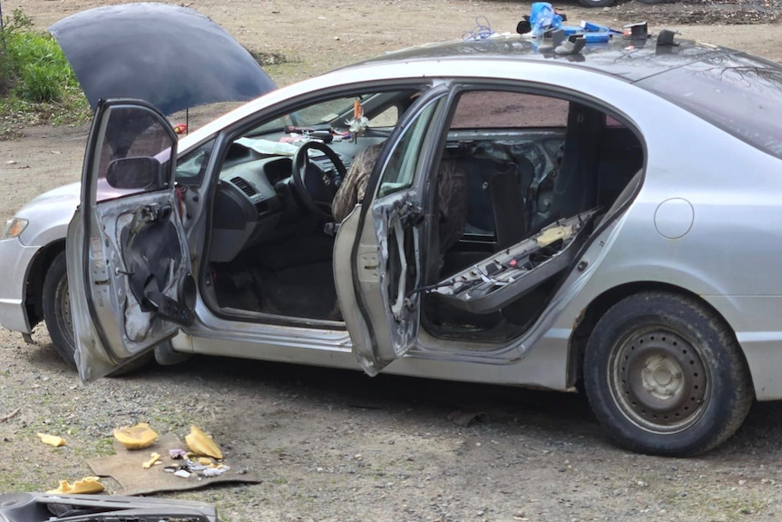 The outsides of a silver sedan with all doors and bonnet open showing damage from a wild bear break in.