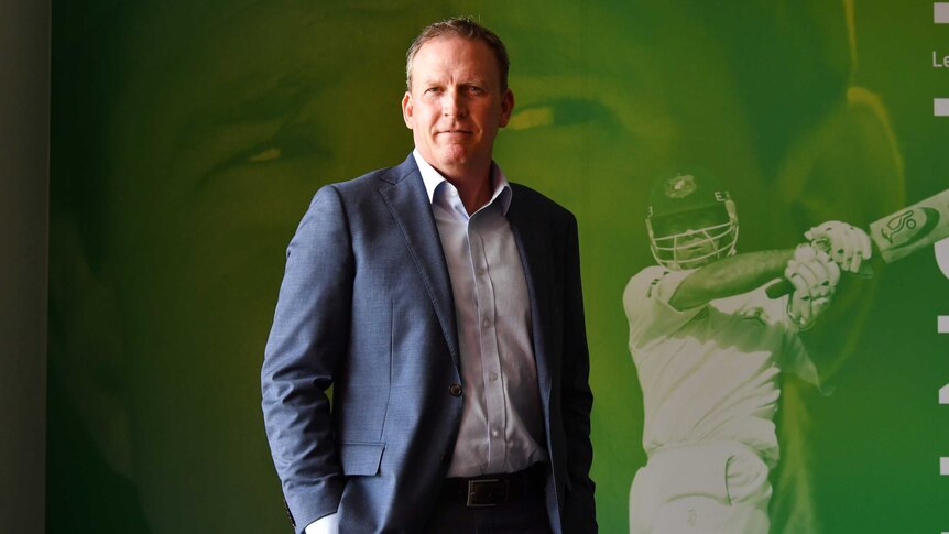 An Australian cricket executive stands in front of a photo portrait of Ricky Ponting.